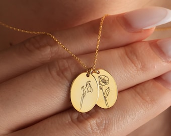 Könnte beinhalten: Eine goldfarbene Halskette mit zwei ovalen Anhängern, die jeweils mit einem floralen Design graviert sind. Die Halskette wird in einer Hand gehalten, wobei die feine Kette und die detaillierten floralen Gravuren auf den Anhängern hervorgehoben werden.