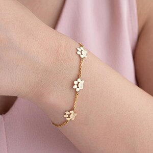 Könnte beinhalten: Ein goldfarbenes Kettenarmband mit drei gleichmäßig verteilten Pfotenabdruck-Anhängern. Jeder Anhänger ist mit einem Namen graviert, namentlich Max, Ben und Jack, die direkt in das Metalldesign der Pfotenform entlang der feinen Gliederkette eingearbeitet sind.