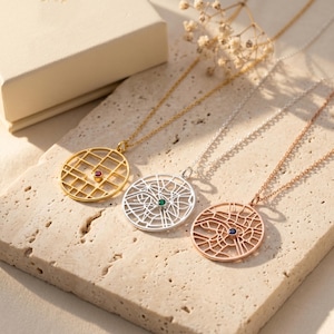 May include: Three circular pendant necklaces featuring a cutout street map design. One gold necklace with a red stone, one silver necklace with a green stone, and one rose gold necklace with a blue stone. Each pendant hangs from a matching chain.