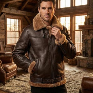 Puede incluir: Chaqueta de cuero marrón con cuello y puños de borrego. La chaqueta tiene cremallera y cinturón en la cintura. El hombre está en un entorno rústico con chimenea y vigas de madera.