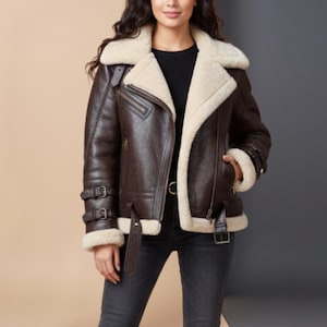 Può includere: Giacca in pelle marrone con fodera e colletto in montone color crema. La giacca presenta una cerniera asimmetrica, fibbie multiple e una cintura in vita. Indossata con jeans neri.