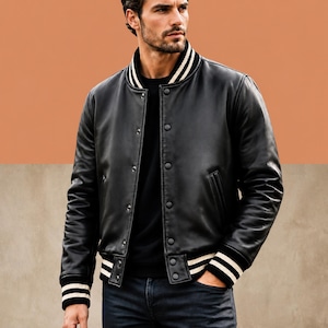 May include: A black leather varsity jacket featuring a snap-button front closure, a ribbed collar with white stripes, and matching ribbed cuffs with white stripes. The jacket has two side pockets and is worn over a plain black shirt and dark jeans.