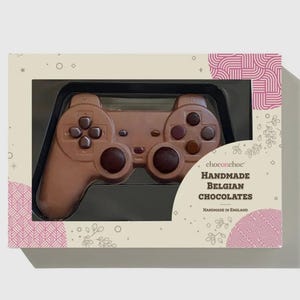 May include: A milk chocolate video game controller presented in a gift box. The chocolate is light brown with darker brown buttons. The box features the text "choconchoc Handmade Belgian Chocolates Handmade in England".