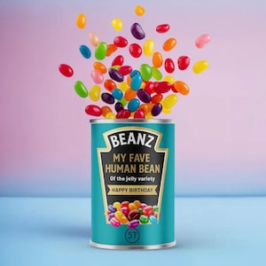May include: A teal tin of "Beanz" with the text "My Fave Human Bean" and "Happy Birthday." Multicoloured jelly beans are spilling out of the tin against a pink and blue background.