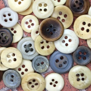 May include: A collection of assorted buttons in various shades of brown, white, and gray. The buttons are made of a smooth, polished material and have a classic, vintage look.