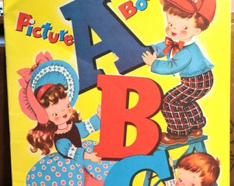 Pode incluir: Um livro de imagens vintage para crianças com uma capa amarela e o título "Picture Book ABC". A capa apresenta três crianças segurando grandes letras coloridas A, B e C. As crianças estão vestidas com roupas coloridas e estão sorrindo.