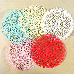 May include: Five round, decorative doilies in various colors, including red, pink, yellow, blue, and white. The doilies have a delicate, intricate design with a floral pattern.