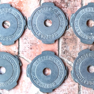 May include: Six gray metal discs with the text "WEBSTER-CHICAGO CORPORATION" around the edge. Each disc has a hole in the center.