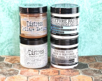 May include: Four jars of craft paint and texture paste. The jars are labeled "Distress Collage Medium - vintage", "Texture Paste Transparent Matte", "Distress Crackle Paint Clear Rock Candy", and "Texture Paste Pâte à Texturer Pasta para Textura".