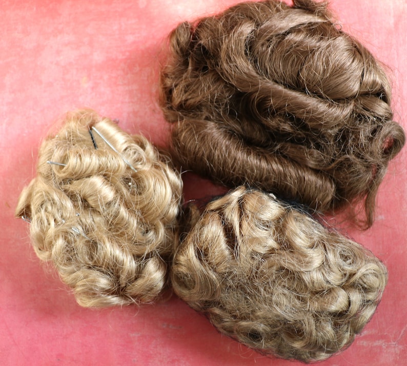 May include: Three hairpieces for doll making. One is brown and the other two are blonde. The blonde hairpieces are curly and the brown hairpiece is wavy.