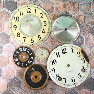 May include: Six vintage clock faces, including a Sessions clock face with Roman numerals, a white clock face with black numbers, and a silver clock face with a black 9. The clock faces are on a hexagonal tile background.