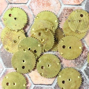 May include: A collection of small, circular brass gears with jagged edges and two or three holes. The gears are scattered on a multi-colored, hexagonal tile surface. The gears are likely vintage watch parts.