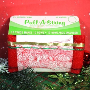May include: A package of red Pull-A-String ribbon, 3.5 inches wide, for making bows. The packaging is white and green with text that reads "Pull-A-String" and "10 yards makes 10 bows". The ribbon is wrapped around the packaging.
