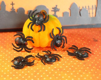 May include: Six black plastic spiders on an orange and white polka dot surface.  One spider is on top of an orange pumpkin.