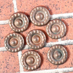 May include: Seven antique-looking copper buttons with a raised center and a decorative, scalloped edge.