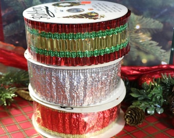 May include: Three rolls of Christmas ribbon. The top roll is red and green with gold glitter. The middle roll is silver with a crinkled texture. The bottom roll is red with gold glitter.