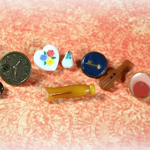 May include: Assortment of vintage buttons in various shapes, colors, and designs, including a clock face, a heart with floral accents, a key, a violin, a ladybug, and a simple circle.