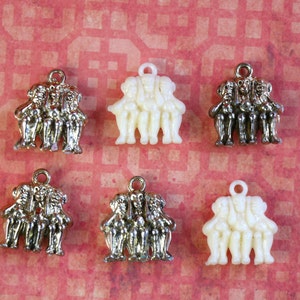 May include: Six charms featuring three figures holding hands, each charm is a different color: gold, white, and black.