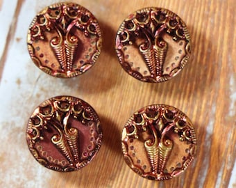 May include: Four ornate, round buttons with a gold and copper finish. The buttons feature a raised, intricate design with a floral motif.