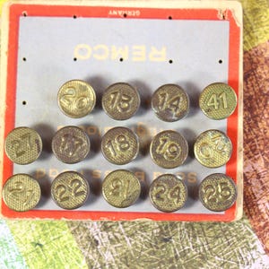May include: A vintage card with 15 numbered brass tacks, each with a different number from 1 to 25. The card is labeled "REMCO" and "GERMANY".