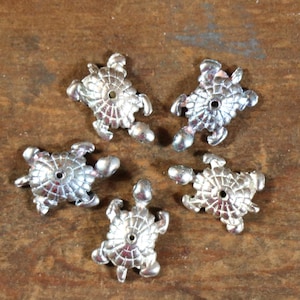 May include: Five silver turtle-shaped charms with a hole in the center. The charms are detailed with a textured shell design.