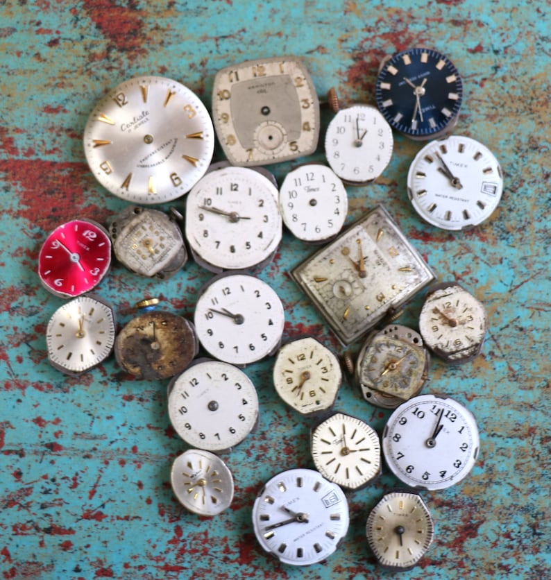 May include: A collection of vintage watch faces in various styles and colours, including silver, gold, white, and black. Some of the faces have Roman numerals, while others have Arabic numerals. The watch faces are arranged on a blue and green textured surface.
