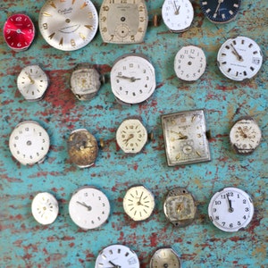 May include: A collection of vintage wristwatches in various styles and colours, including silver, gold, and black. Some watches have Roman numeral markings, while others have Arabic numerals. The watches are arranged on a blue and green textured surface.