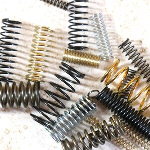 May include: Assortment of metal springs in various sizes and colors, including gold, silver, and black.