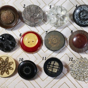 May include: Twelve assorted buttons in various colors, materials, and designs. The buttons are arranged in three rows of four buttons each. The buttons are all round and have a diameter of approximately 1 inch.
