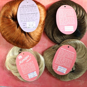 May include: Four brown, blonde, and red hairpieces with attached tags. The tags include washing instructions and product information, such as the style, size, and color. The text on the tags reads "Monique Collection", "Baby Boy", "Teen Wispy", and "Teen Wispy".