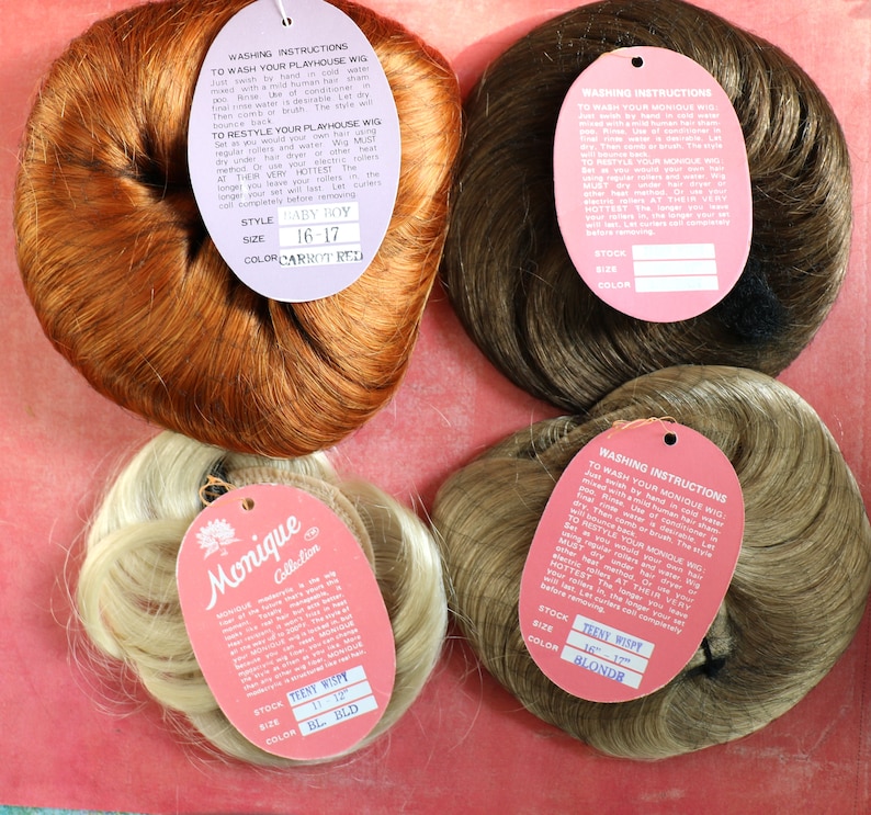 May include: Four brown, blonde, and red hairpieces with attached tags. The tags include washing instructions and product information, such as the style, size, and color. The text on the tags reads "Monique Collection", "Baby Boy", "Teen Wispy", and "Teen Wispy".