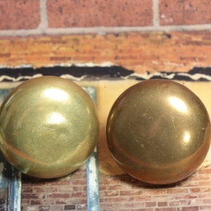 May include: Two round, gold-colored metal buttons. The buttons are smooth and shiny.