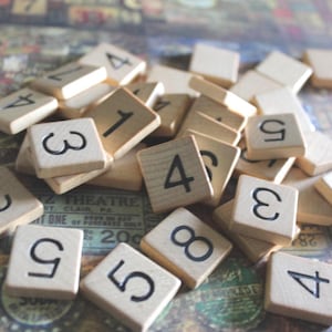 May include: A close-up of a pile of wooden tiles with numbers printed on them. The tiles are arranged in a random order, with some numbers overlapping. The tiles are on a textured surface.