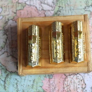 Op de afbeelding: Drie gouden miniatuurtreinlocomotieven in een houten doos. De locomotieven hebben ingewikkelde details en zijn in een rij gerangschikt.