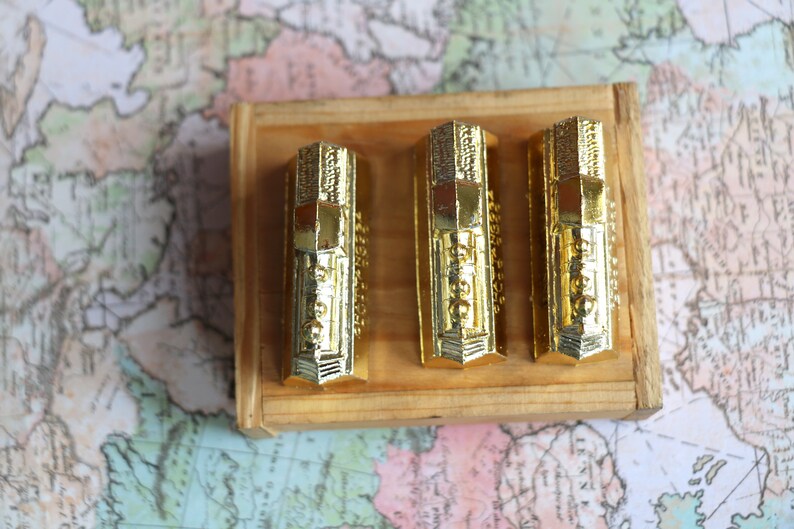 Op de afbeelding: Drie gouden miniatuurtreinlocomotieven in een houten doos. De locomotieven hebben ingewikkelde details en zijn in een rij gerangschikt.