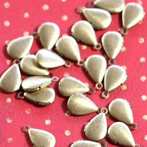 May include: A group of 20 gold-toned teardrop-shaped metal charms with a hinged opening. The charms are scattered on a red background with white polka dots.