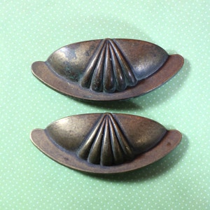 May include: Two antique brass cabinet pulls with a scalloped design. The pulls are in the shape of a half-circle and have a smooth, worn finish.