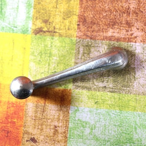 May include: A silver metal car door handle with a round knob. The handle is on a colorful checkered background.
