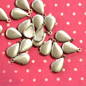 May include: A group of 20 gold teardrop-shaped metal charms with a small loop at the top. The charms are scattered on a red background with white polka dots.