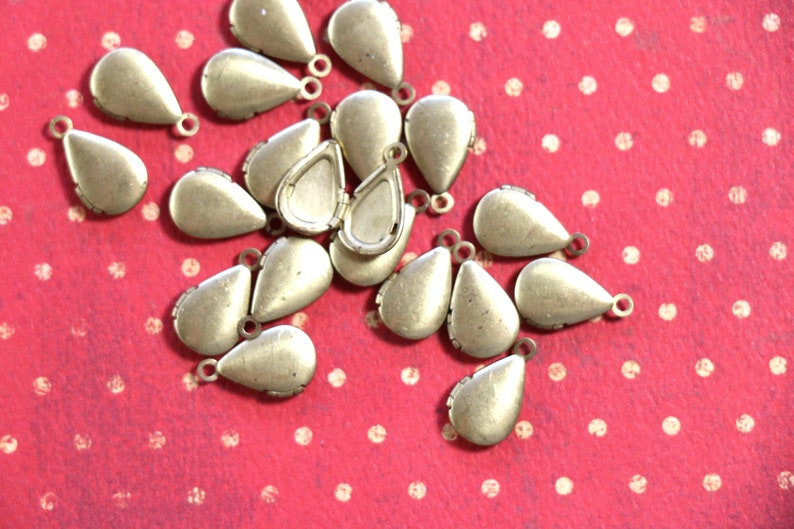 May include: A group of 20 gold teardrop-shaped metal charms with a small loop at the top. The charms are scattered on a red background with white polka dots.