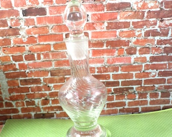 May include: A clear glass bottle with a textured surface and a round stopper. The bottle has a bulbous body and a narrow neck.