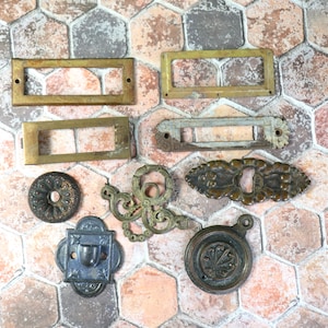 May include: Assortment of vintage brass and metal hardware pieces, including door plates, knobs, and decorative accents. The pieces have a rustic, aged look and are perfect for adding a touch of vintage charm to any home decor project.