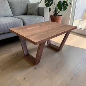 May include: A rectangular wooden coffee table with a rich brown finish. The table features a unique V-shaped leg design, adding a modern touch to the living room furniture. The table is approximately 40 inches long and 20 inches wide.