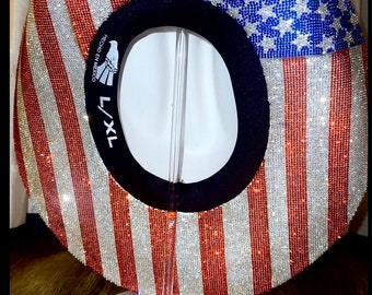 Puede incluir: Un sombrero vaquero rojo, blanco y azul con pedrería, con un patrón de estrellas en la corona y rayas en el ala. El sombrero está en un soporte de exhibición y tiene una etiqueta que dice "HECHO EN MEXICO L/XL".