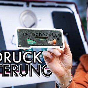 Peut inclure: Un support noir imprimé en 3D avec le texte "abgecheckt.co" est présenté devant un écran d'ordinateur. Le support a un design géométrique avec des découpes et un circuit imprimé vert visible. Les mots "3D DRUCK HALTERUNG" sont au premier plan.