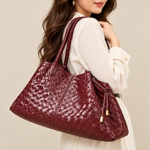 Può includere: Una borsa tote color bordeaux intenso caratterizzata da un intricato motivo in pelle intrecciata su tutto l'esterno. La borsa include due tracolle intrecciate abbinate e un dettaglio con coulisse laterale rifinito con accenti in metallo dorato.