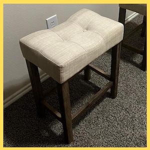 May include: A white ceramic mug with a black handle and the text "But First, Coffee" in a bold, black font. The mug is set against a blurred background, suggesting a cozy setting. The mug appears to be approximately 4 inches tall.