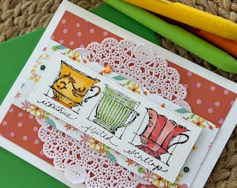 May include: A handmade greeting card featuring watercolor illustrations of teacups labeled "Icanthus", "Fluted", and "Scallop". The card has a white lace doily, orange polka dot background, and three colorful pens.