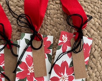 May include: Four red and white gift tags with a floral design. Each tag has a brown paper label and is tied with black twine and a red ribbon.