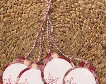 May include: Four circular gift tags with a red and beige plaid border and a white center featuring a small red poinsettia illustration. Each tag has a hole at the top with a red and white twisted twine string attached for hanging purposes.